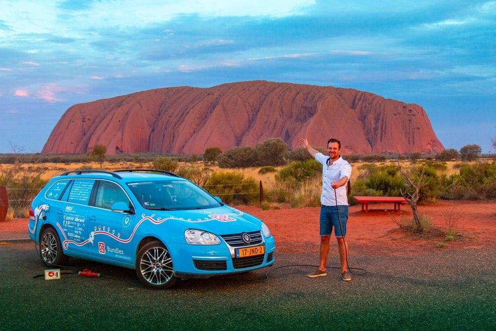 Mit Elektroauto vor dem Uluru Berg in Australien